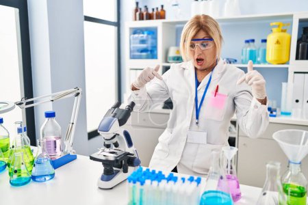 Photo for Middle age blonde woman working at scientist laboratory pointing down with fingers showing advertisement, surprised face and open mouth - Royalty Free Image