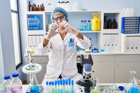 Photo for Brunette woman working at scientist laboratory smiling in love doing heart symbol shape with hands. romantic concept. - Royalty Free Image