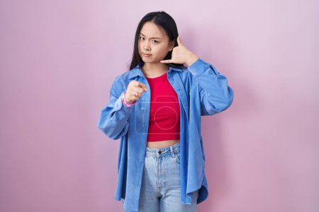 Téléchargez les photos : Jeune femme asiatique debout sur fond rose souriant faire parler au téléphone geste et vous pointant du doigt. Appelle-moi. - en image libre de droit