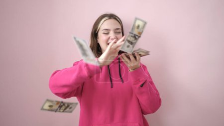 Téléchargez les photos : Jeune femme blonde souriant confiant jeter des dollars sur fond rose isolé - en image libre de droit