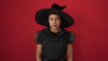 Photo for African american woman wearing witch costume having halloween party over isolated red background - Royalty Free Image