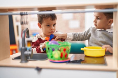 Téléchargez les photos : Deux enfants jouent avec la cuisine de jeu debout à la maternelle - en image libre de droit