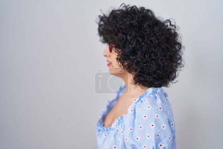 Photo for Young brunette woman with curly hair wearing glasses over isolated background looking to side, relax profile pose with natural face with confident smile. - Royalty Free Image