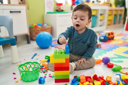 Foto de Adorable niño hispano jugando con bloques de construcción sentado en el suelo en el jardín de infantes - Imagen libre de derechos
