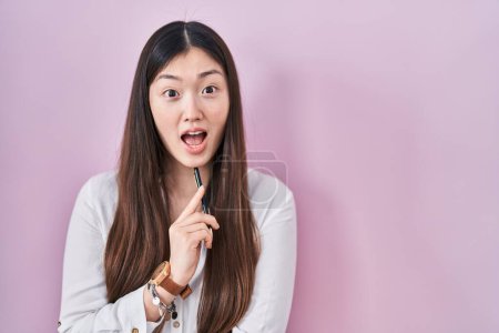 Photo for Chinese young woman holding pencil over pink background celebrating crazy and amazed for success with open eyes screaming excited. - Royalty Free Image