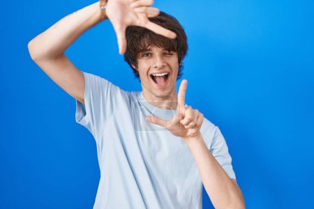 Photo for Hispanic young man standing over blue background smiling making frame with hands and fingers with happy face. creativity and photography concept. - Royalty Free Image