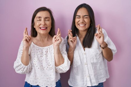 Téléchargez les photos : Mère hispanique et fille ensemble geste doigt croisé souriant avec espoir et les yeux fermés. chance et concept superstitieux. - en image libre de droit