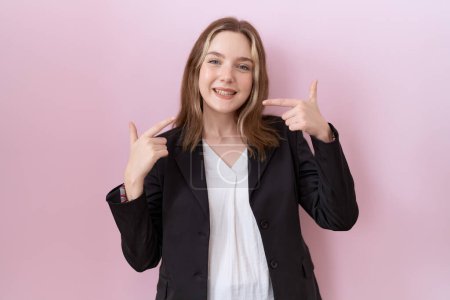 Téléchargez les photos : Jeune femme d'affaires caucasienne portant une veste noire souriante et joyeuse montrant et pointant du doigt les dents et la bouche. concept de santé dentaire. - en image libre de droit