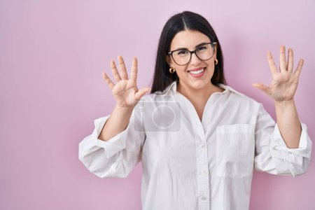 Photo for Young brunette woman standing over pink background showing and pointing up with fingers number ten while smiling confident and happy. - Royalty Free Image