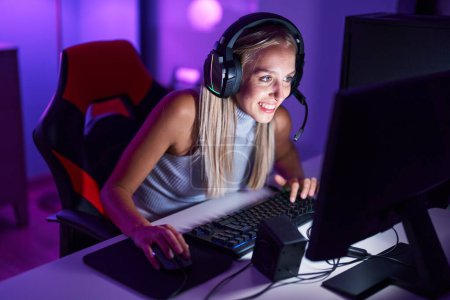 Foto de Joven mujer rubia streamer jugando videojuego utilizando el ordenador en la sala de juegos - Imagen libre de derechos