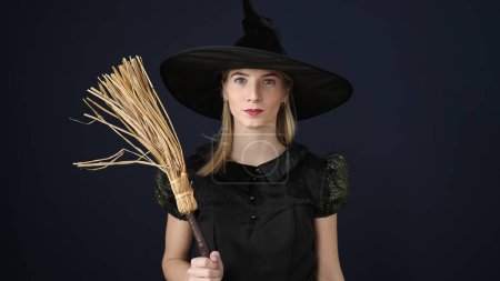Photo for Young blonde woman wearing witch costume holding broom over isolated black background - Royalty Free Image