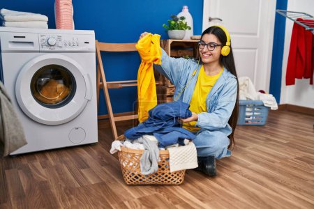 Téléchargez les photos : Young hispanic woman listening to music waiting for washing machine at laundry room - en image libre de droit