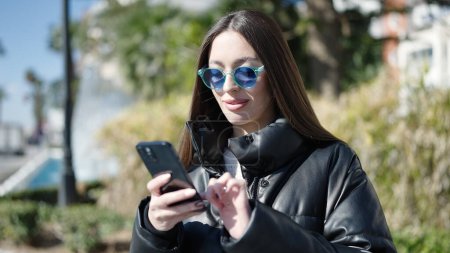 Photo for Young beautiful hispanic woman smiling confident using smartphone at park - Royalty Free Image