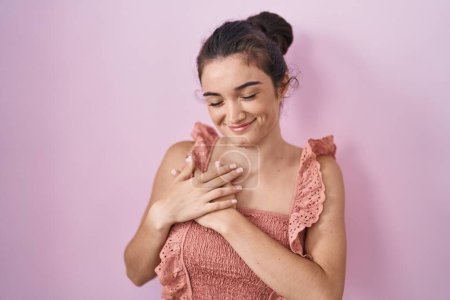 Téléchargez les photos : Young teenager girl standing over pink background smiling with hands on chest with closed eyes and grateful gesture on face. health concept. - en image libre de droit