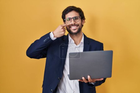 Téléchargez les photos : Beau latin homme travaillant à l'aide d'un ordinateur portable pointant avec le doigt de la main au visage et au nez, souriant gai. concept de beauté - en image libre de droit