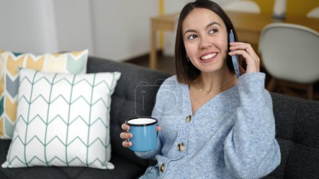 Téléchargez les photos : Jeune belle femme hispanique parlant sur smartphone boire du café à la maison - en image libre de droit