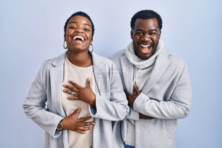 Foto de Joven pareja afroamericana de pie sobre fondo azul juntos sonriendo y riendo en voz alta porque divertida broma loca con las manos en el cuerpo. - Imagen libre de derechos