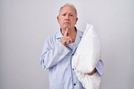 Photo for Senior man with grey hair wearing pijama hugging pillow thinking concentrated about doubt with finger on chin and looking up wondering - Royalty Free Image