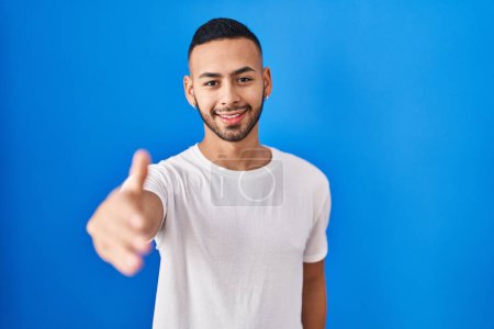 Téléchargez les photos : Jeune homme hispanique debout sur fond bleu souriant joyeuse offrant main de paume donnant assistance et acceptation. - en image libre de droit