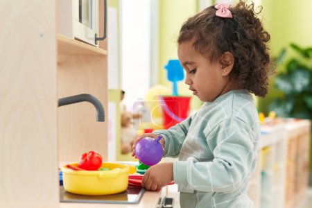 Téléchargez les photos : Adorable fille hispanique jouant avec la cuisine de jeu debout à la maternelle - en image libre de droit