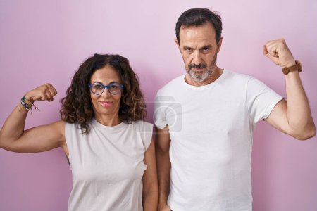 Foto de Mediana edad pareja hispana juntos sobre rosa fondo fuerte persona mostrando brazo músculo, confiado y orgulloso de poder - Imagen libre de derechos