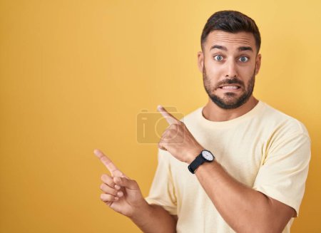 Photo pour Handsome hispanic man standing over yellow background pointing aside worried and nervous with both hands, concerned and surprised expression - image libre de droit