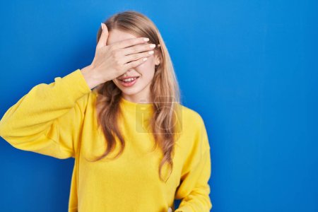 Photo for Young caucasian woman standing over blue background smiling and laughing with hand on face covering eyes for surprise. blind concept. - Royalty Free Image