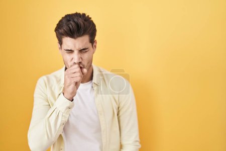 Foto de Hombre hispano joven parado sobre fondo amarillo sintiéndose mal y tosiendo como síntoma de resfriado o bronquitis. concepto de atención sanitaria. - Imagen libre de derechos