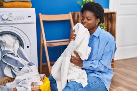 Photo for African american woman smelling towel using washing machine at laundry room - Royalty Free Image
