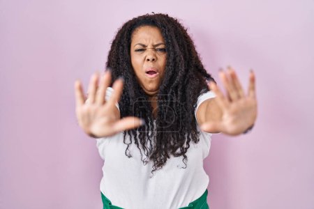 Foto de Más tamaño mujer hispana de pie sobre fondo rosa haciendo gesto de stop con las manos palmas, enojado y expresión de frustración - Imagen libre de derechos