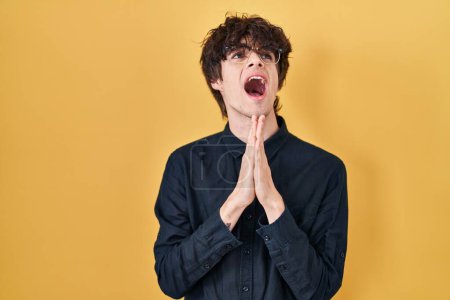 Photo for Young man wearing glasses over yellow background begging and praying with hands together with hope expression on face very emotional and worried. begging. - Royalty Free Image
