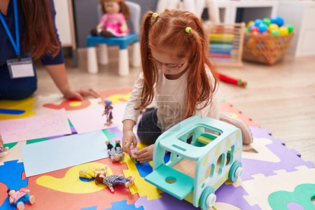 Téléchargez les photos : Adorable rousse fille jouer avec des jouets assis sur le sol à la maternelle - en image libre de droit