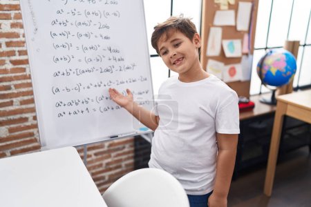 Photo for Adorable hispanic boy smiling confident standing by chalkboard with maths exercise at classroom - Royalty Free Image