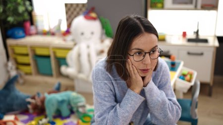 Photo for Young beautiful hispanic woman teacher sitting on table with stressed expression at kindergarten - Royalty Free Image