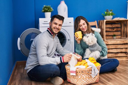 Photo for Man and woman drinking coffee washing clothes with dog at laundry room - Royalty Free Image