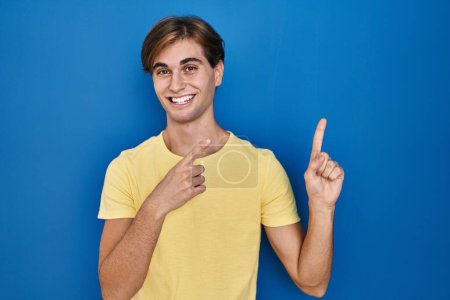 Photo for Young man standing over blue background smiling and looking at the camera pointing with two hands and fingers to the side. - Royalty Free Image