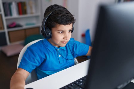 Téléchargez les photos : Adorable hispanic boy student using computer sitting on table at classroom - en image libre de droit