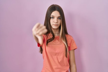 Foto de Adolescente chica de pie sobre fondo rosa buscando infeliz y enojado mostrando rechazo y negativo con los pulgares hacia abajo gesto. mala expresión. - Imagen libre de derechos