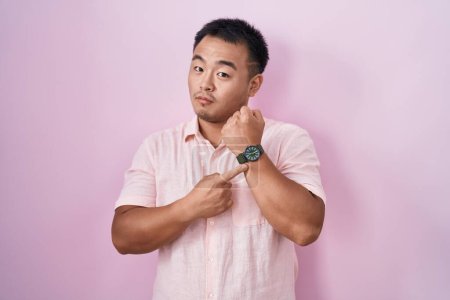 Téléchargez les photos : Jeune homme chinois debout sur fond rose pressé pointant vers regarder le temps, l'impatience, regardant la caméra avec une expression détendue - en image libre de droit