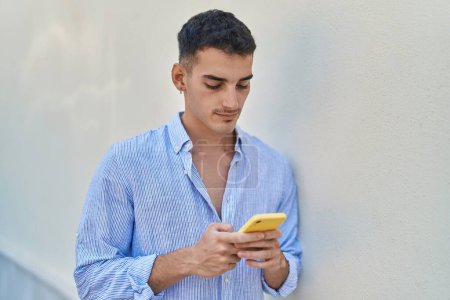Foto de Hombre hispano joven usando smartphone con expresión seria sobre fondo blanco aislado - Imagen libre de derechos