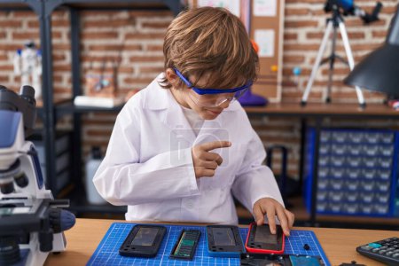 Photo for Adorable caucasian boy scientist repairing smartphone at classroom - Royalty Free Image