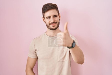 Téléchargez les photos : Homme hispanique avec la barbe debout sur fond rose regardant fier, souriant faire les pouces vers le haut geste sur le côté - en image libre de droit