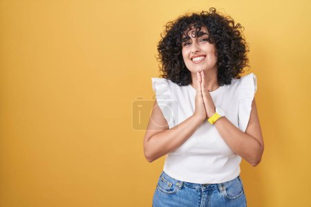 Photo for Young middle east woman standing over yellow background praying with hands together asking for forgiveness smiling confident. - Royalty Free Image