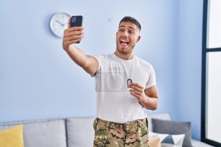 Photo for Young hispanic man wearing camouflage army uniform taking selfie at home celebrating crazy and amazed for success with open eyes screaming excited. - Royalty Free Image