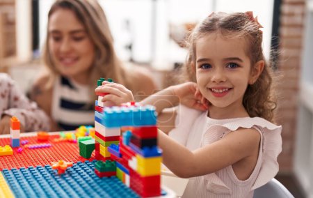 Foto de Profesor y niño pequeño jugando con bloques de construcción sentados en la mesa en el jardín de infantes - Imagen libre de derechos