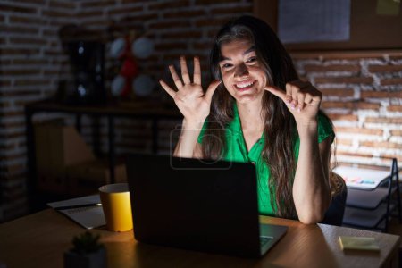 Téléchargez les photos : Young teenager girl working at the office at night showing and pointing up with fingers number six while smiling confident and happy. - en image libre de droit