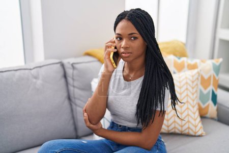Photo for African american woman talking on smartphone with serious expression at home - Royalty Free Image