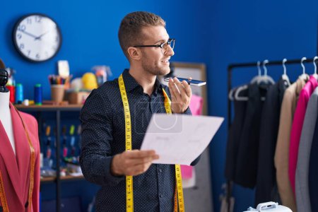 Téléchargez les photos : Young caucasian man tailor talking on smartphone reading document at clothing factory - en image libre de droit