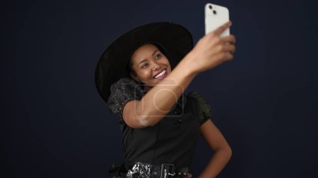 Téléchargez les photos : Femme afro-américaine portant costume de sorcière faire selfie par smartphone sur fond noir isolé - en image libre de droit