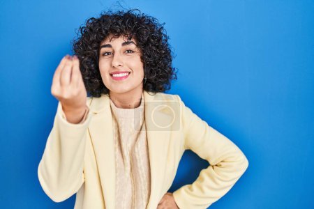 Photo for Young brunette woman with curly hair standing over blue background doing italian gesture with hand and fingers confident expression - Royalty Free Image